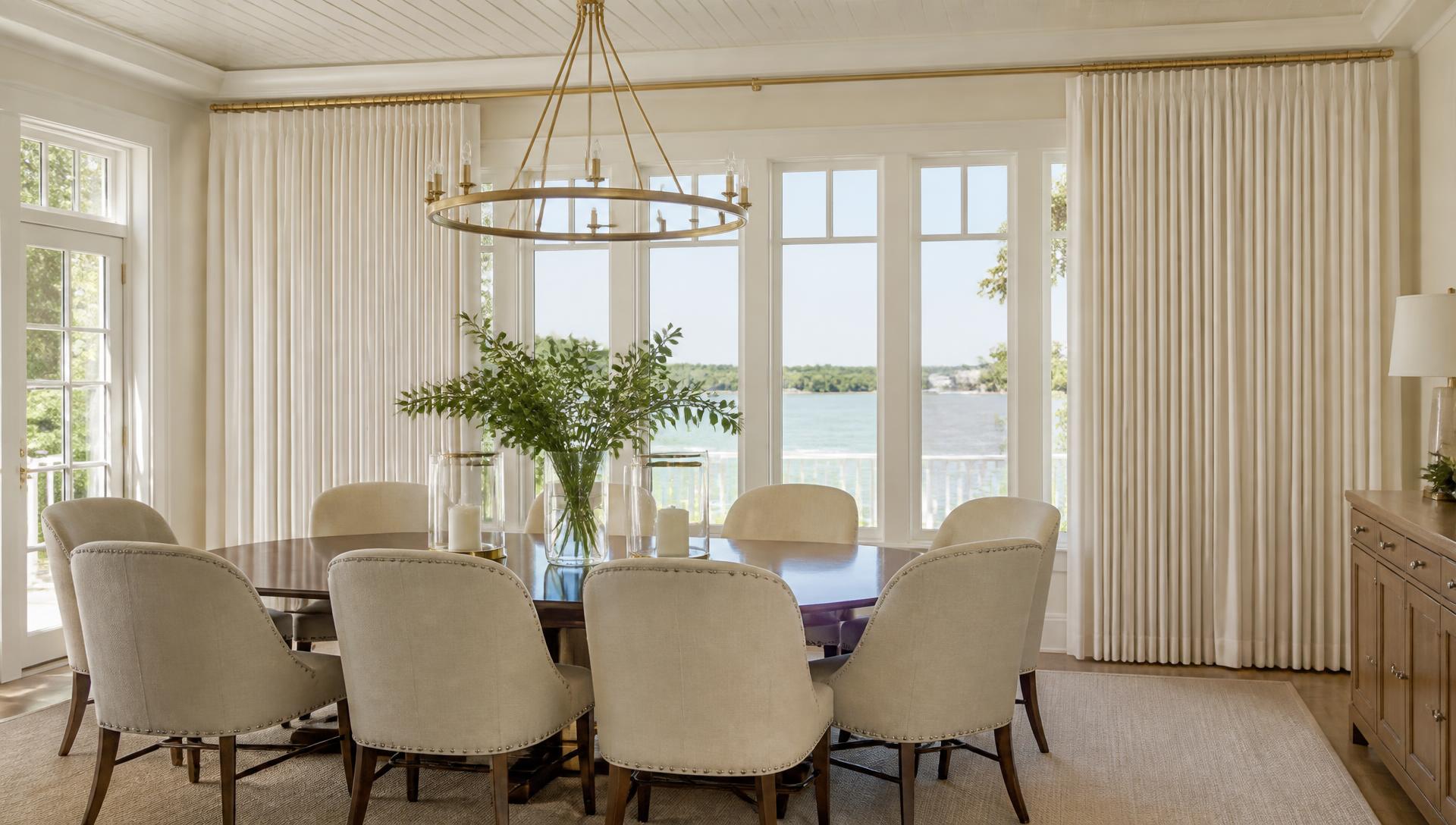 Floor-to-ceiling custom pleated drapery with brass hardware in a waterfront dining room